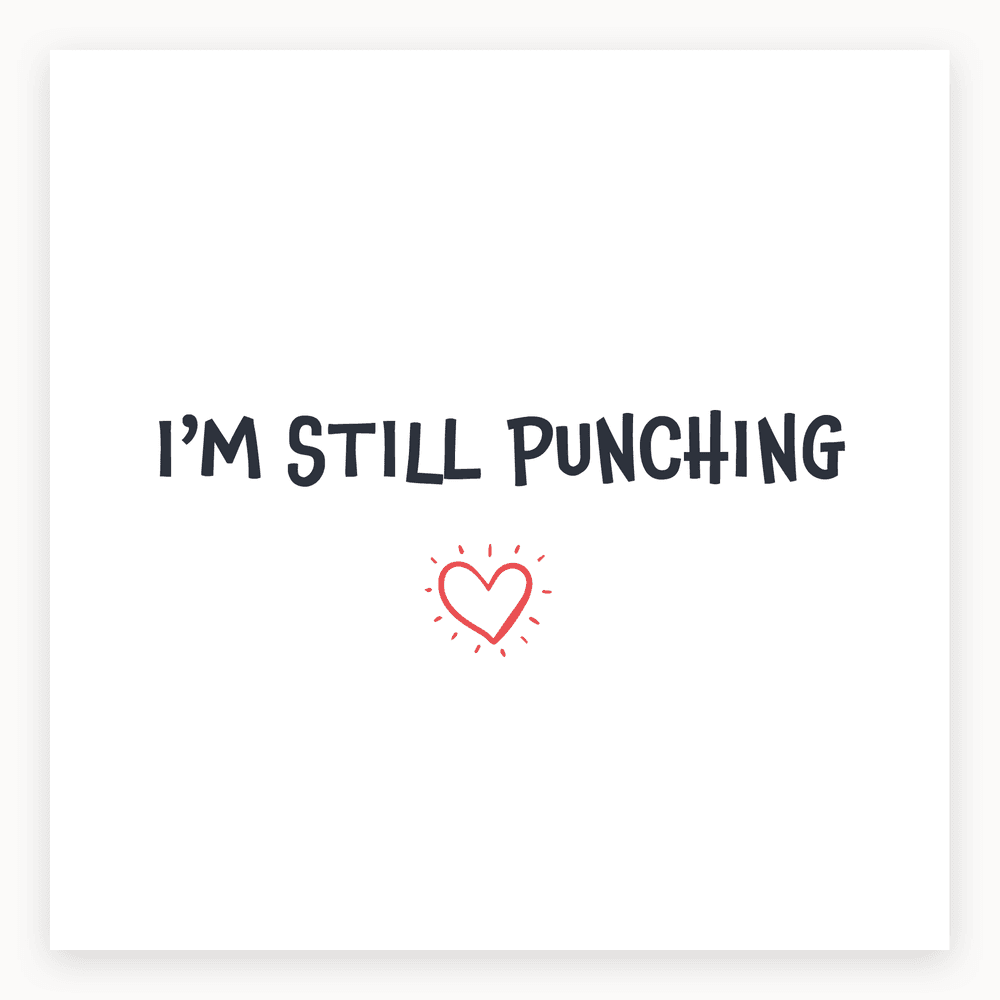 The card lying flat. Card with bold text 'I'M STILL PUNCHING' and a small heart illustration, in red and white.